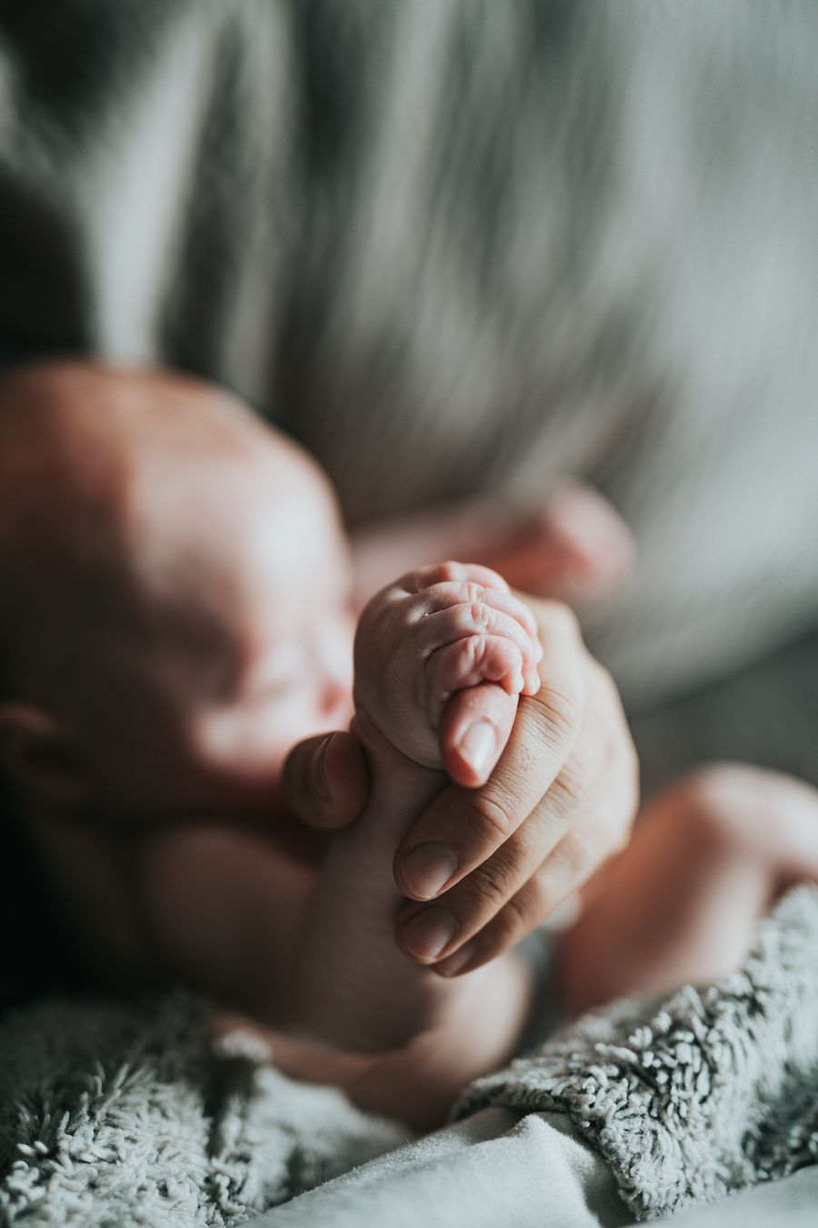 A newborn baby holding an adult's finger